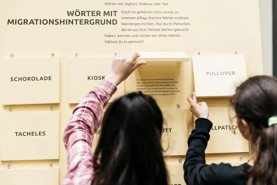 Zwei junge Mädchen stehen vor einer Infotafel auf der Wörter erklärt werden 