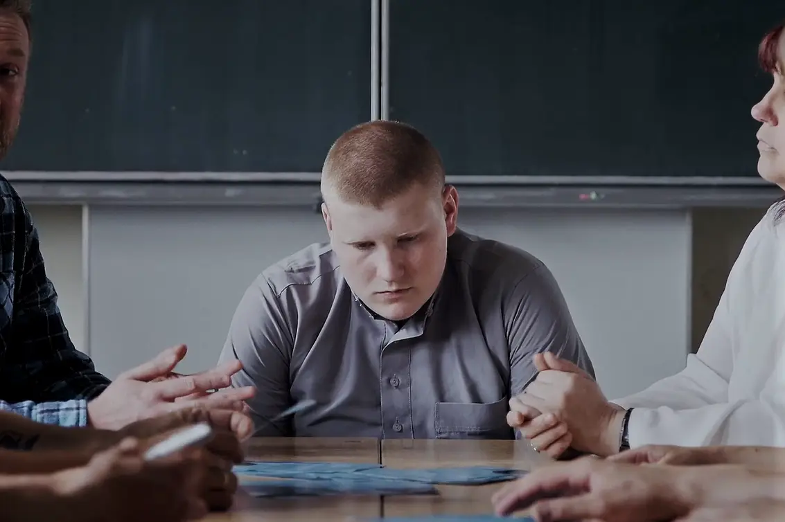 Ein junger Mann sitzt an einem Tisch vor einer Schultafel