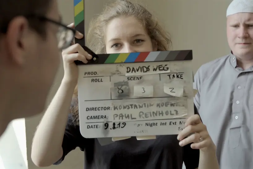 Junges Mädchen hält eine Filmklappe vor ihr Gesicht