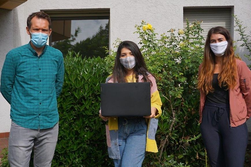 Ein Mann und zwei Frauen bei der Übergabe eines Laptops