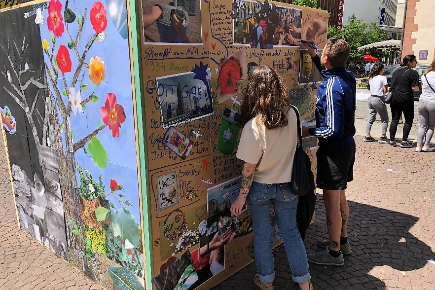 Zwei Jugendliche schreiben auf eine Wand eines hölzernen Kubus 