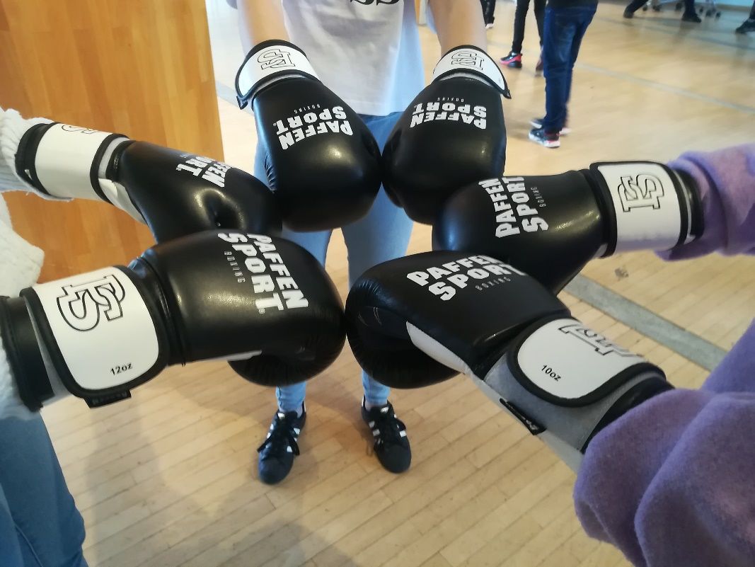 Drei Personen strecken sich ihre mit Boxhandschuhen bedeckten Hände entgegen.