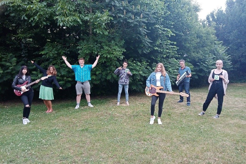 Eine Gruppe von 7 jungen Leuten musiziert auf einer Wiese