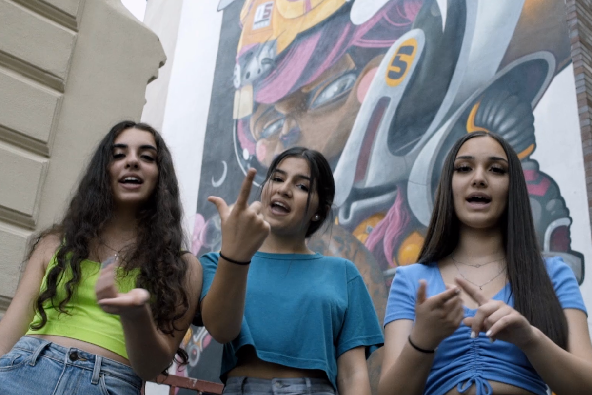 Drei junge Mädchen stehen singend vor einer graffiti Wand
