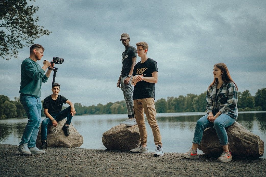 Vier junge Menschen werden an einem See beim singen und rappen fotogrfiert