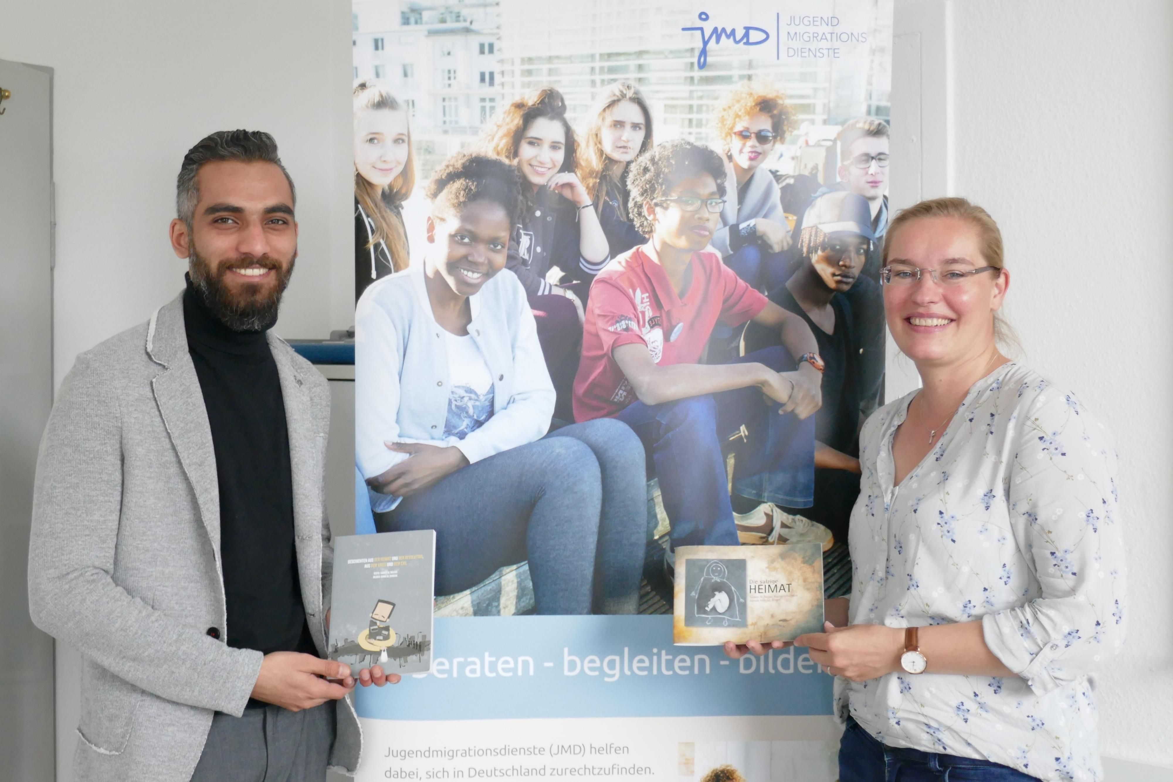 Frau Klocke und Herr Najjar stehen vor einem Plakat des JMD und beide halten das Buch von Herrrn Najjar in der Hand