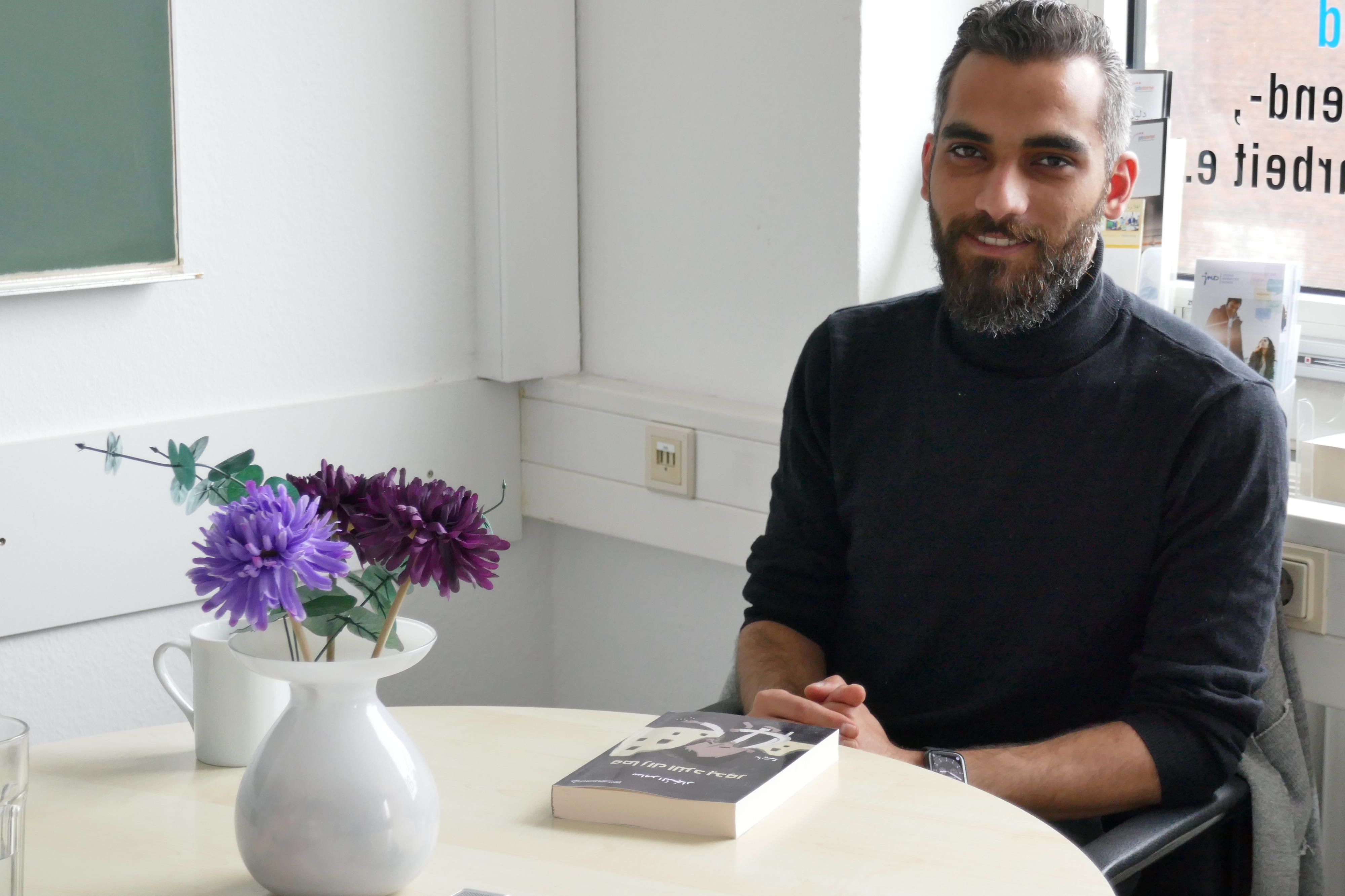 Herr Najjar sitzt an einem Tisch und hat sein Buch vor sich auf dem Tisch liegen