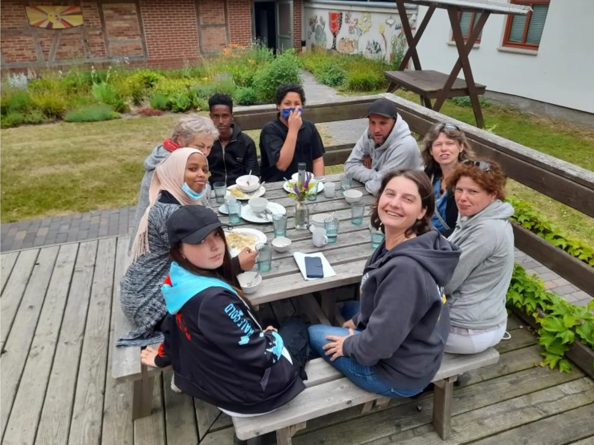 Neun junge Menschen sitzen an einem gedeckten Tisch.