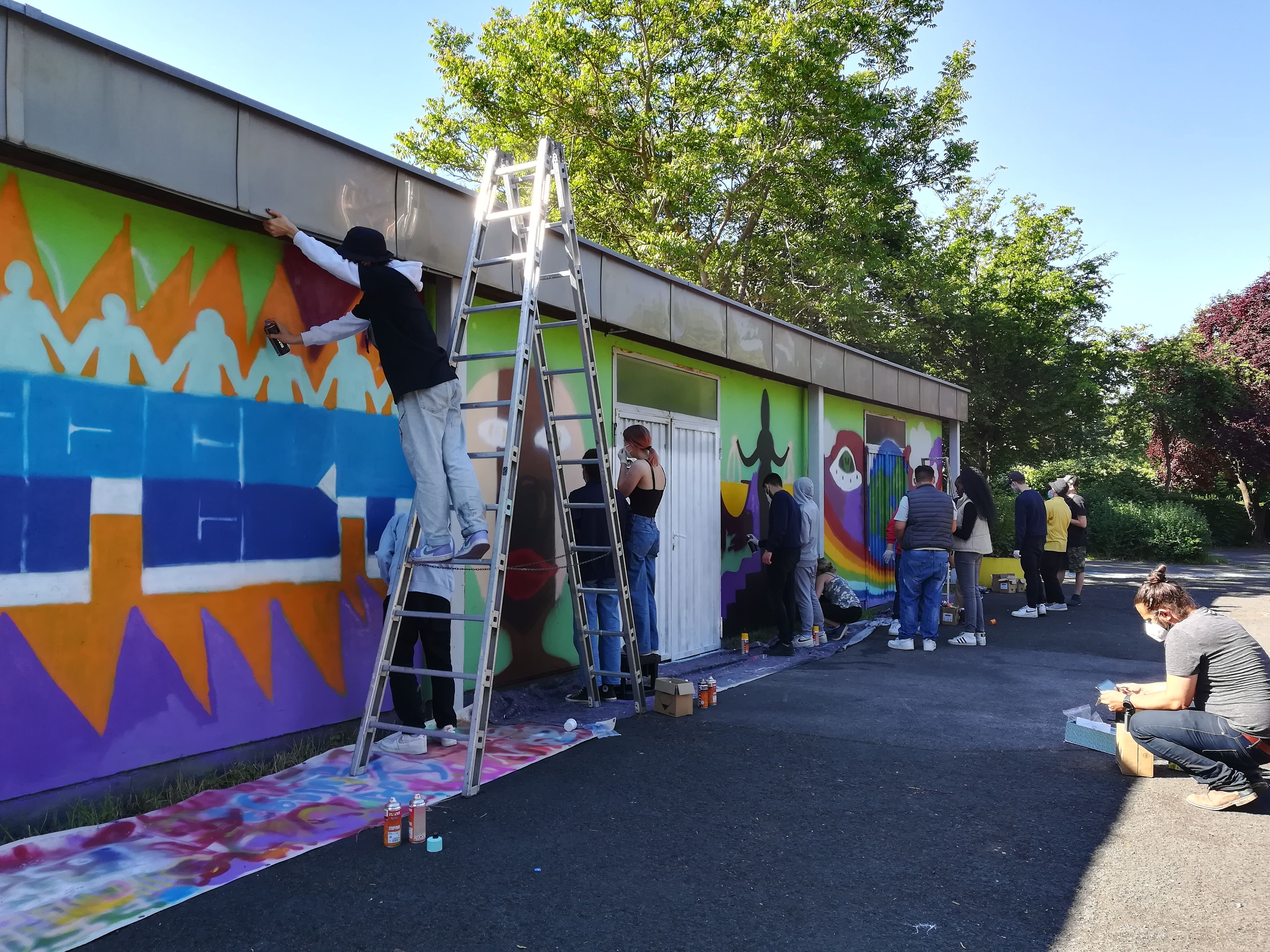 Junge Menschen besprühen mit Graffiti eine Wand.