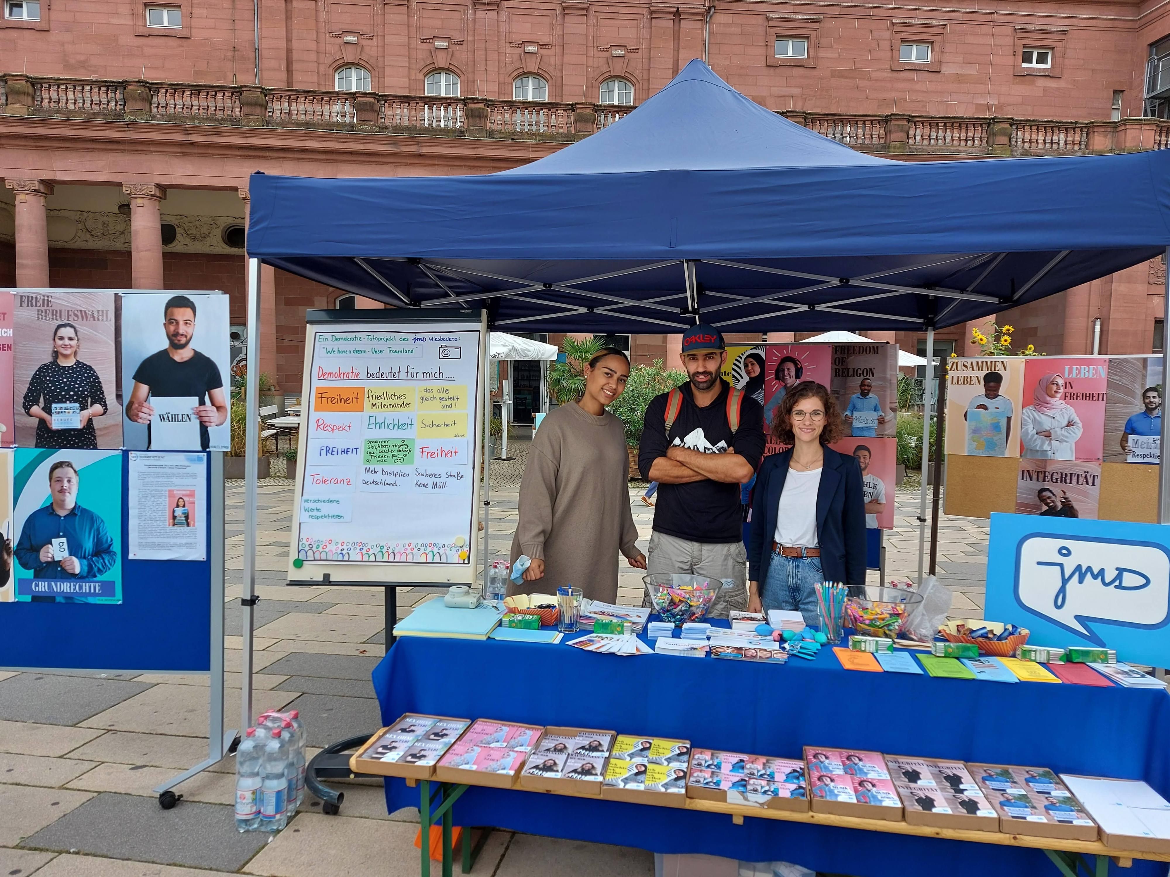 Drei junge Menschen stehen an einem Stand.