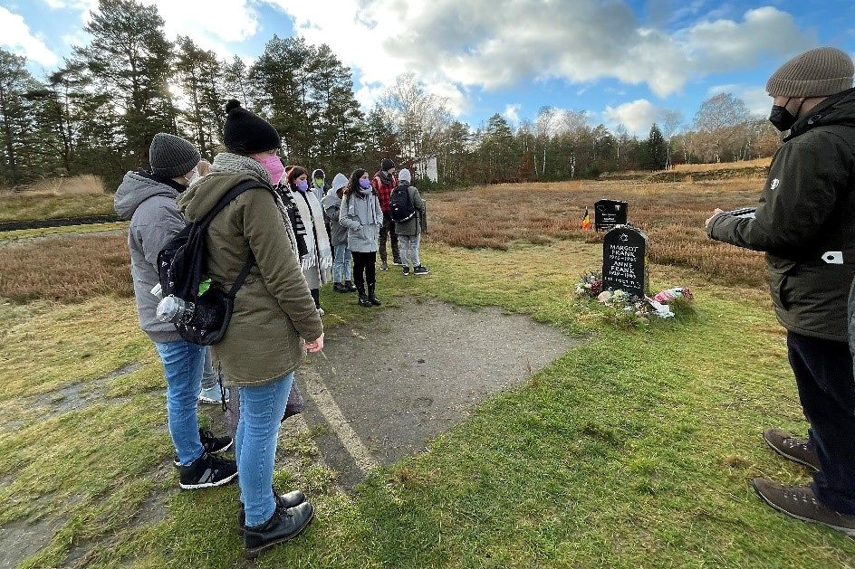 Eine große Gruppe von jungen Menschen steht vor dem Grabstein von Anne Frank