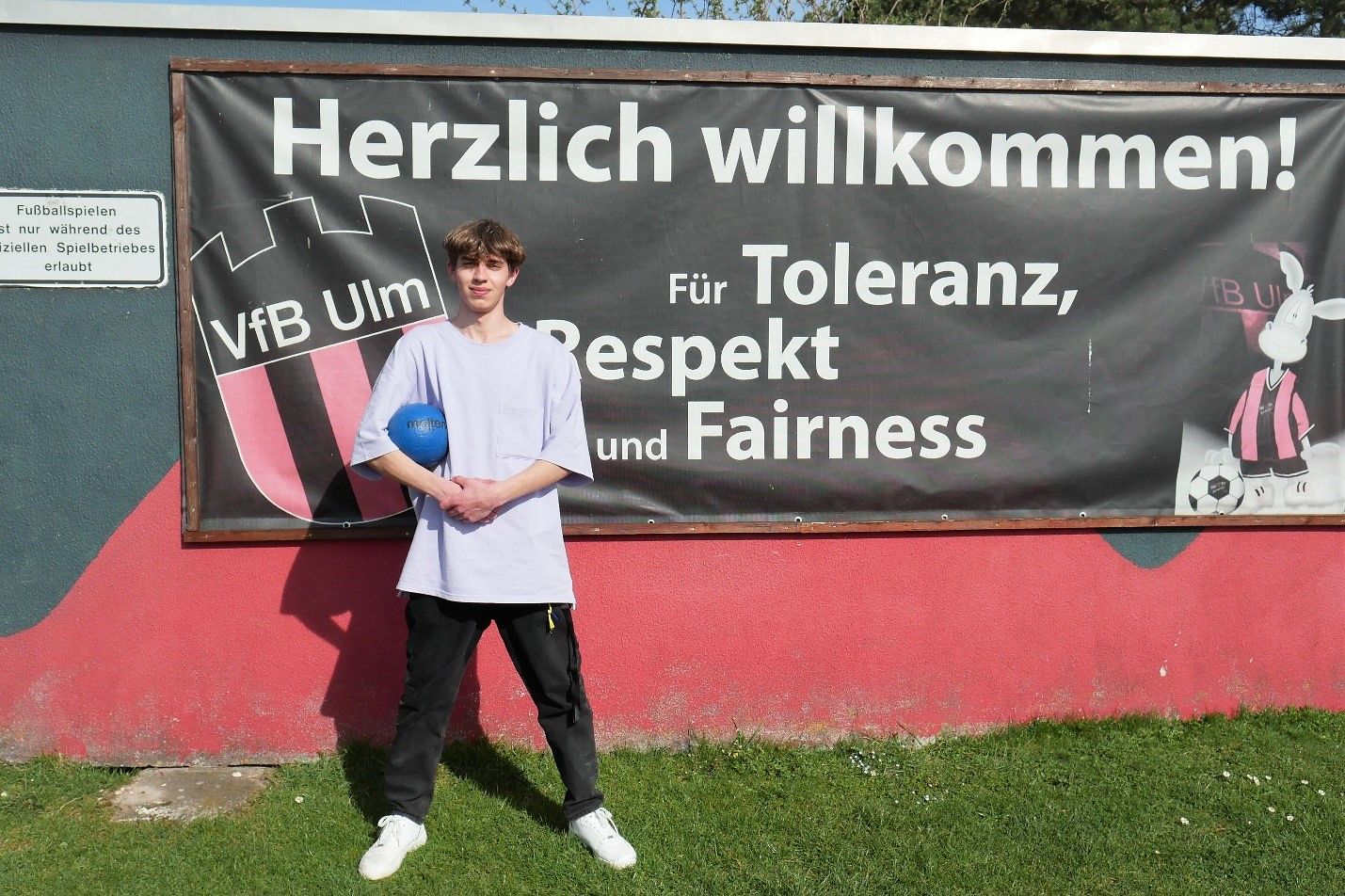 Ein jumger Mann steht vor einem Banner des VfB Ulm