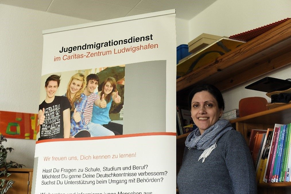 Frau Zahra Hassanpour steht neben einem Banner vom Jugendmigrationsdienst Ludwigshafen