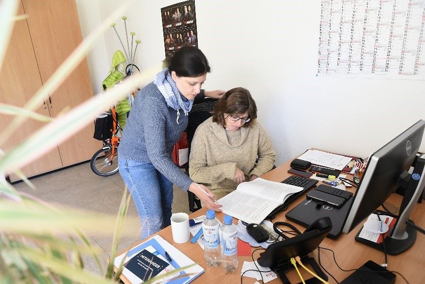 Frau Hassanpour und eine Kollegin an einem Schreibtisch im Austausch.