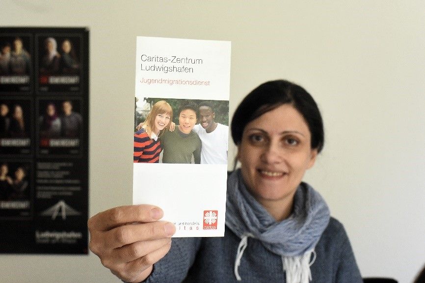 Frau Hassanpour hält einen Flyer vom Jugendmigrationsdienst Ludwigshafen hoch