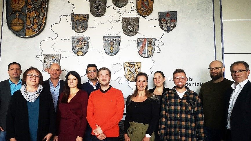 11 Personen stehen vor einer Wand wo eine Karte vom Landkreis Lichtenfels mit Wappen drauf ist.