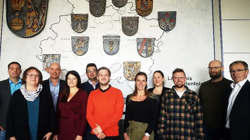 11 Personen stehen vor einer Wand wo eine Karte vom Landkreis Lichtenfels mit Wappen drauf ist.