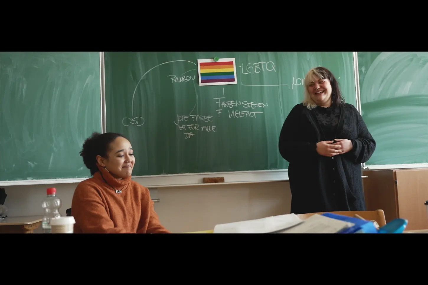 Eine Jugendliche und eine Frau in einem Klasenraum vor einer Tafel.