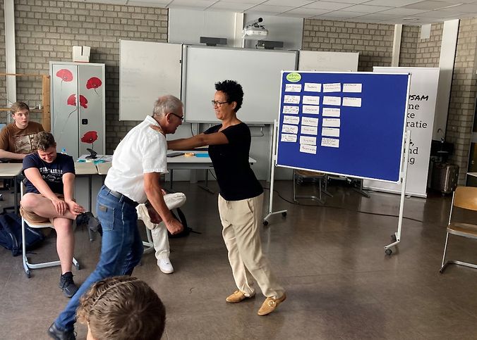 Eine Frau und eine Mann stehen in einem Klassenraum mit Schülern.