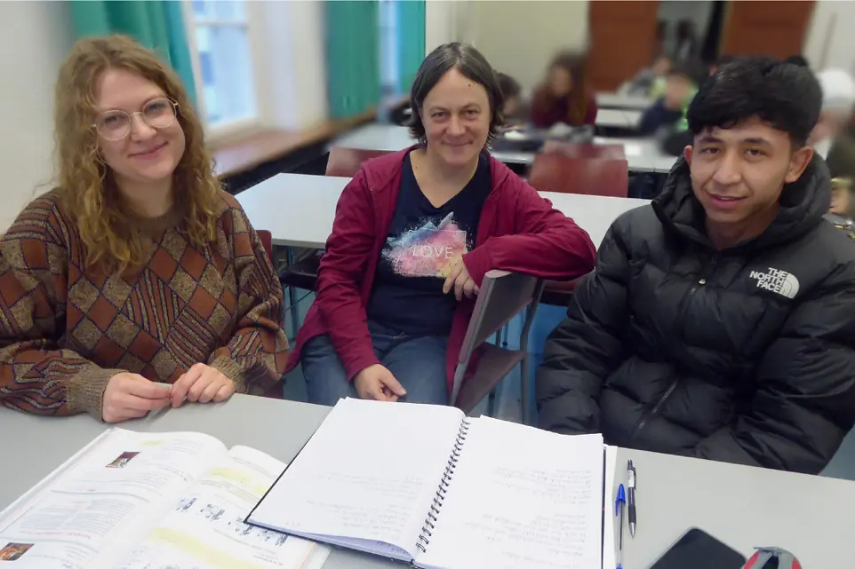 Ein junger Erwachsener und zwei Frauen sitzen an einem Tisch.