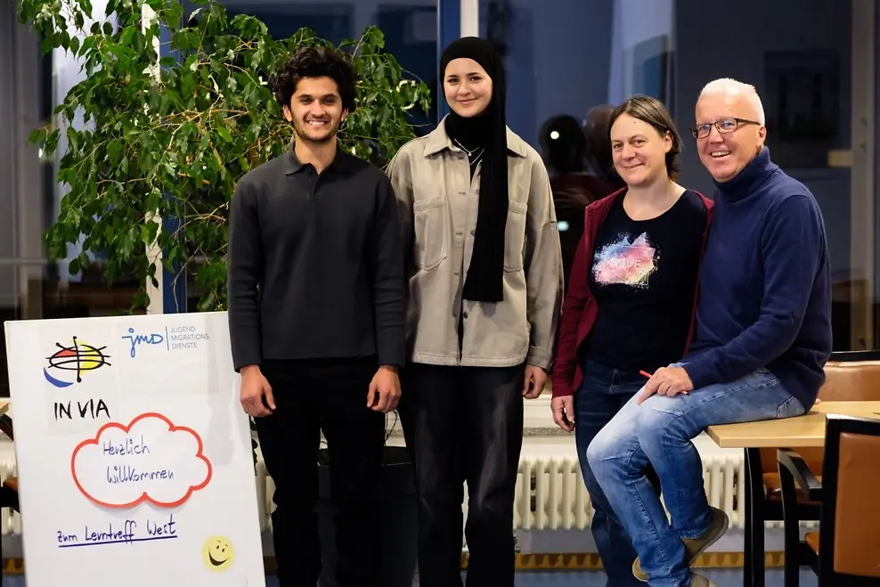 Zwei Frauen und zwei Männer neben einem Plakat.
