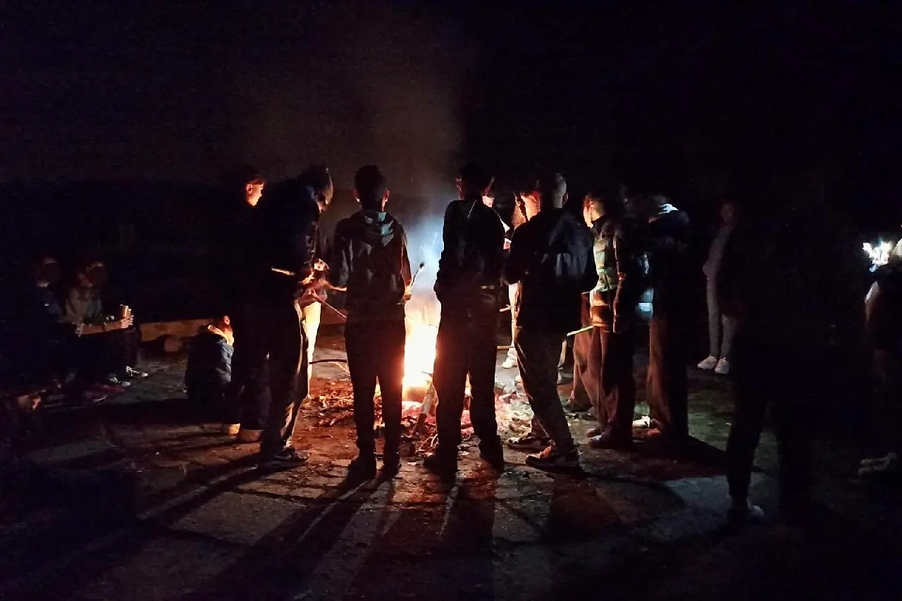 Gruppe Schüler*innen sitzen und stehen um eine Lagerfeuer.