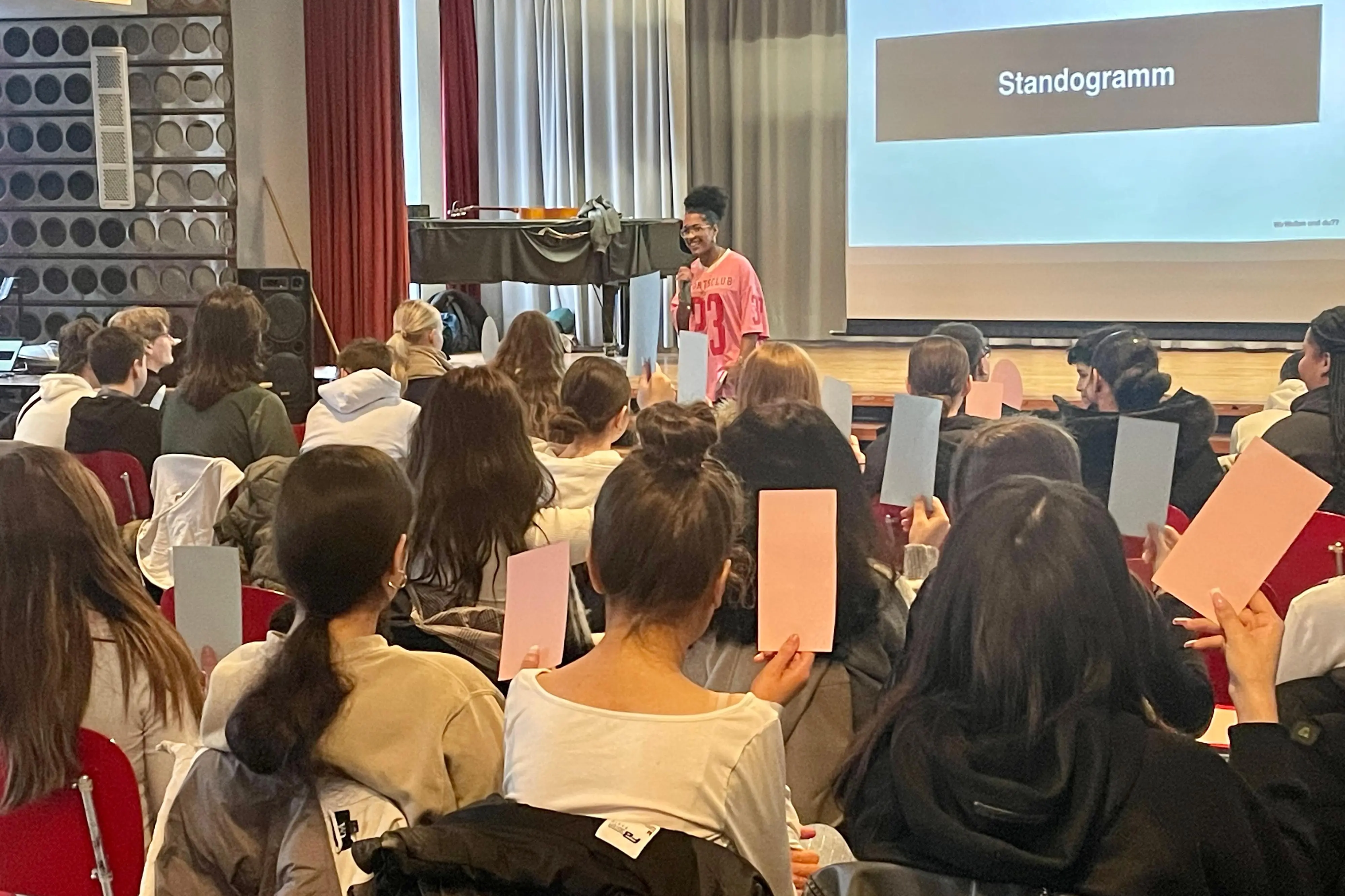 Eine Frau steht vor einer großen Gruppe und stellt Fragen.