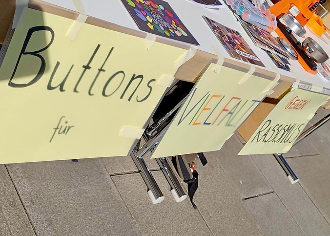An einem Tisch hängt der Text, Buttons für Vielfalt gegen Rassismus 