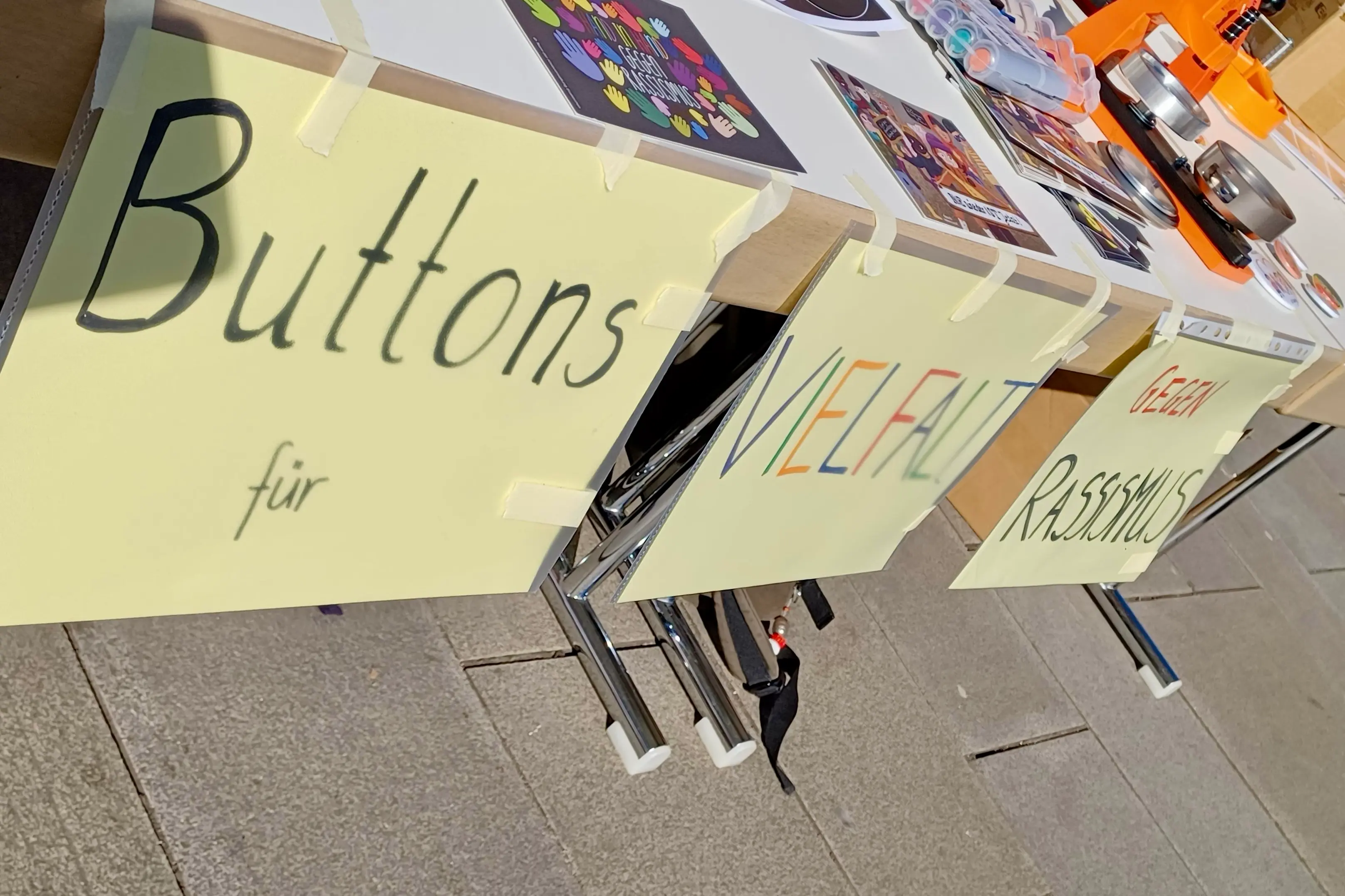 An einem Tisch hängt der Text, Buttons für Vielfalt gegen Rassismus 