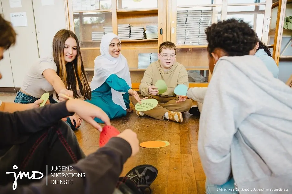 Eine kleine Gruppe von Jungen und Mädchen sitzen im Kreis auf dem Boden und diskutieren.