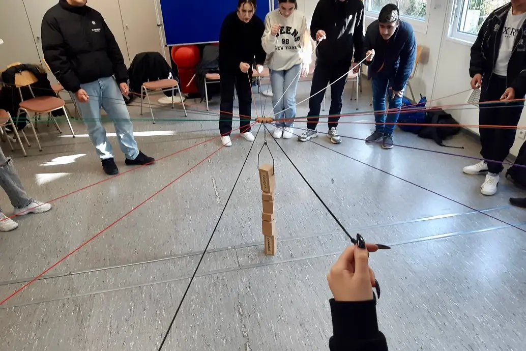 Eine Gruppe von Schülern versucht mit Fäden einen Turm aus Holzklötzen zu bauen.