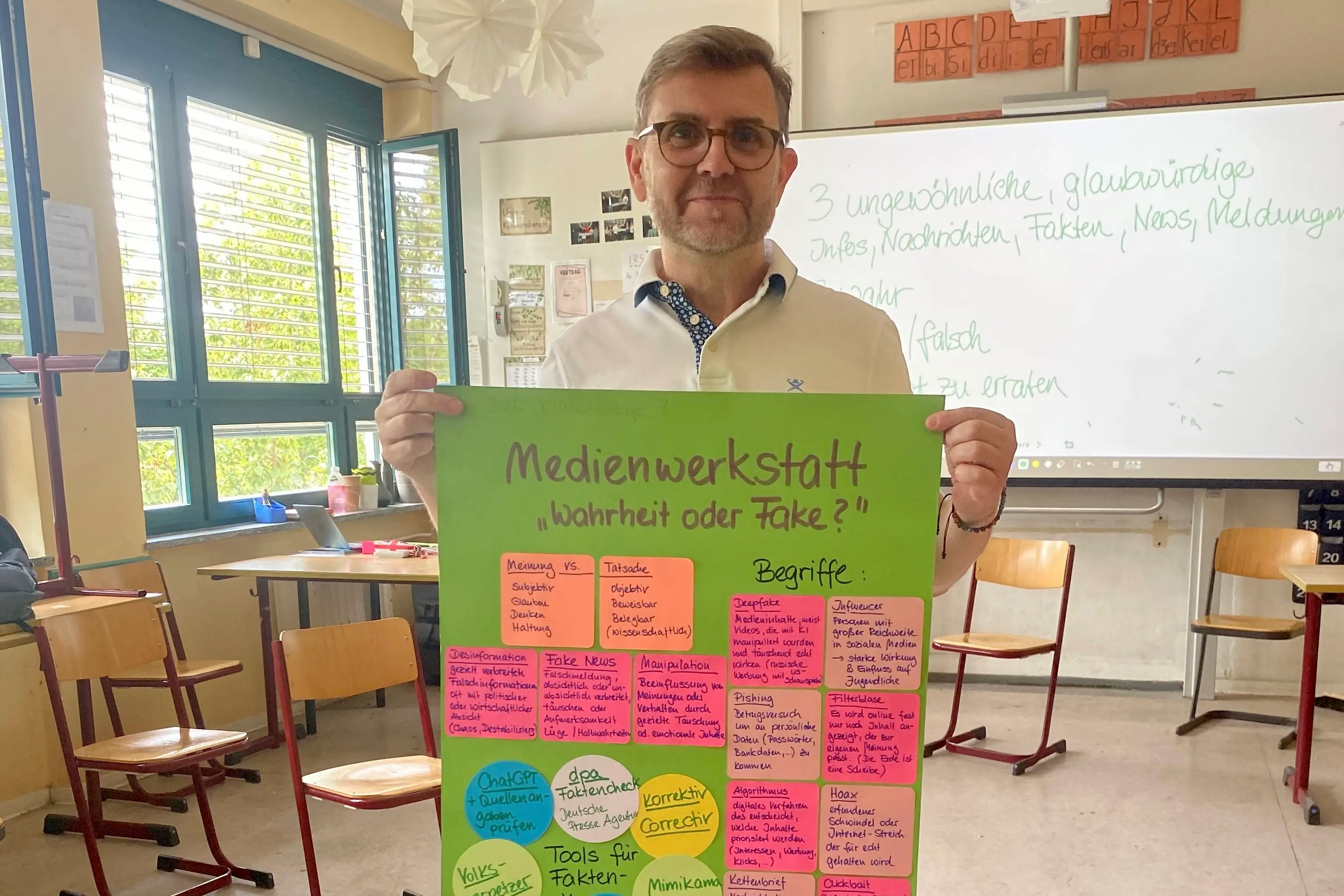Ein Mann steht in einem Klassenraum und hält ein Plakat auf dem die Erkenntnisse aus dem Workshop stehen in der Hand.