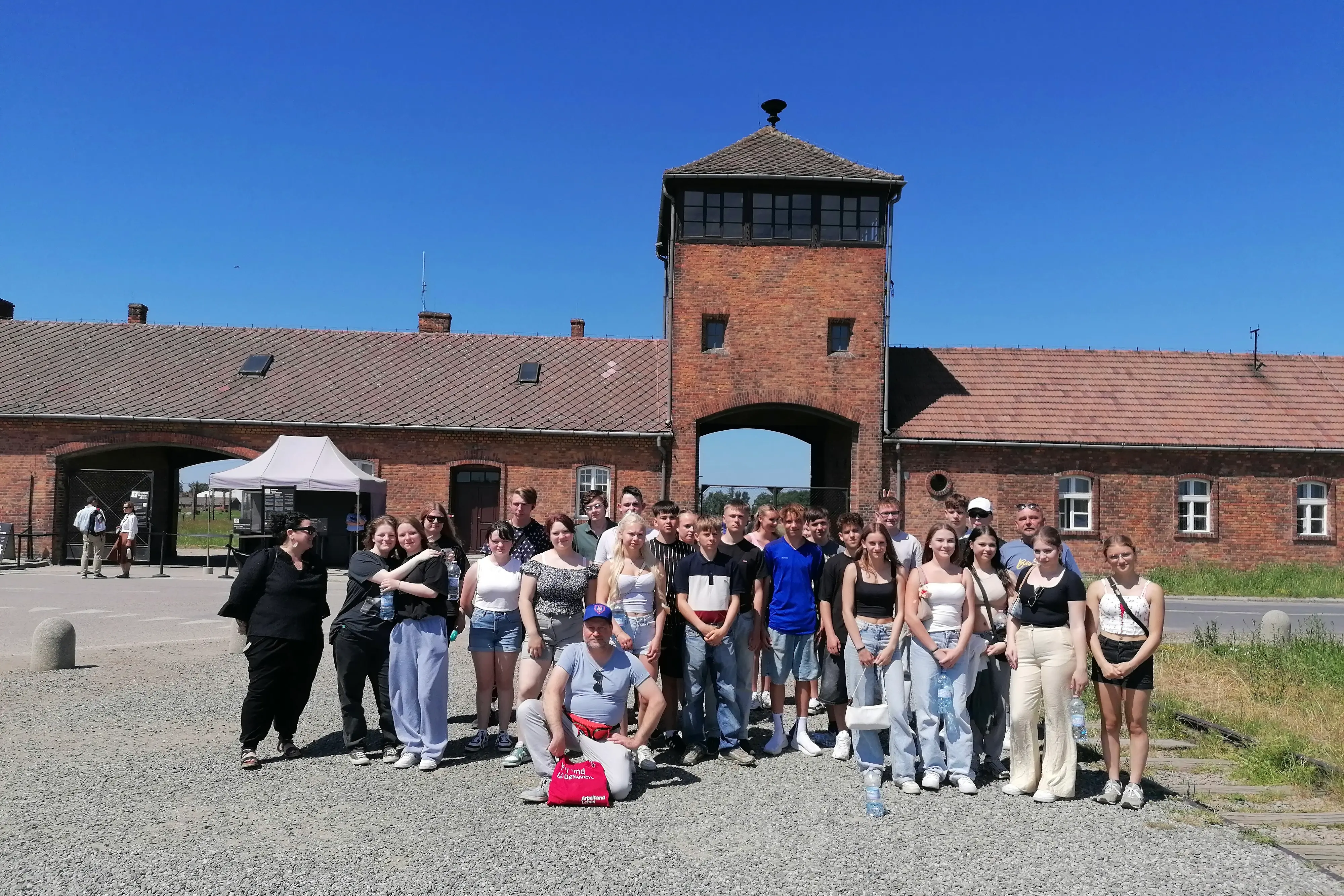 Eine Gruppe steht vor der Gedenkstätte Auschwitz-Birkenau.