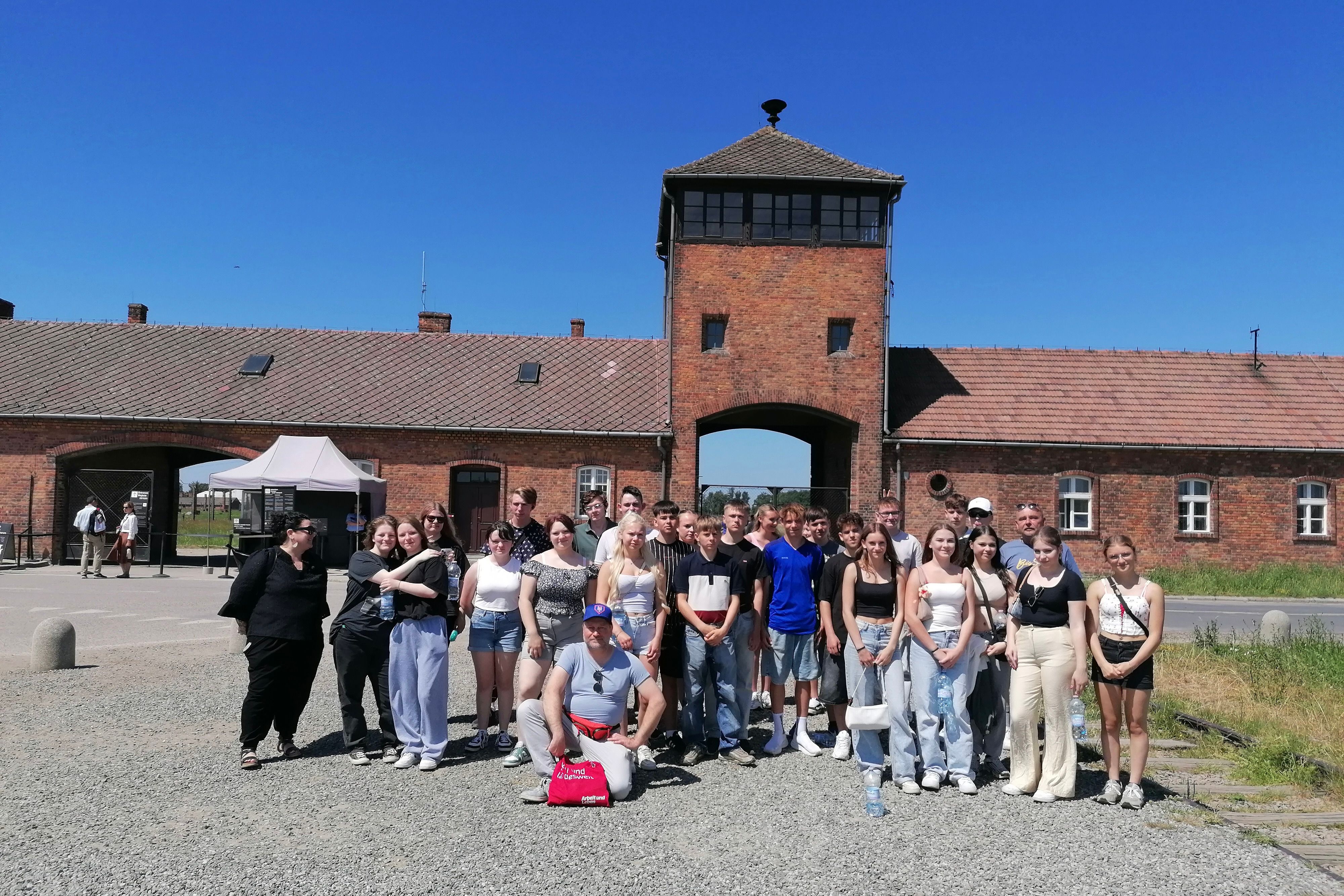 Eine Gruppe steht vor der Gedenkstätte Auschwitz-Birkenau.
