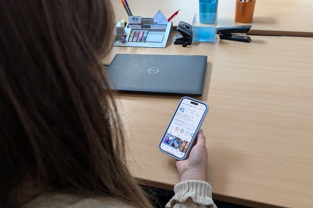 Ein Schreibtisch mit einem Laptop und eine Frau die ein Handy in der Hand hält.