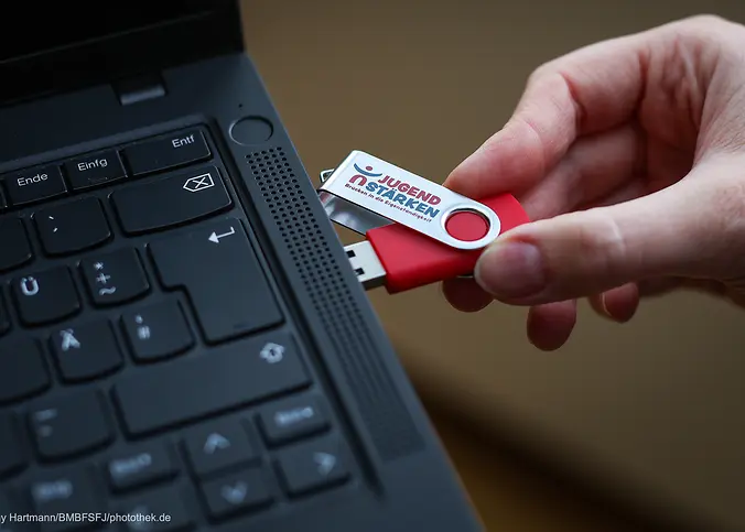 Eine Ecke von einem Laptop, in den ein USB-Stick gesteckt wird.