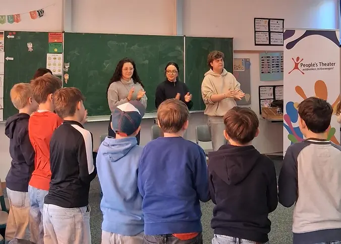 Eine Gruppe steht in einer Klasse vor einer Tafel im Kreis.