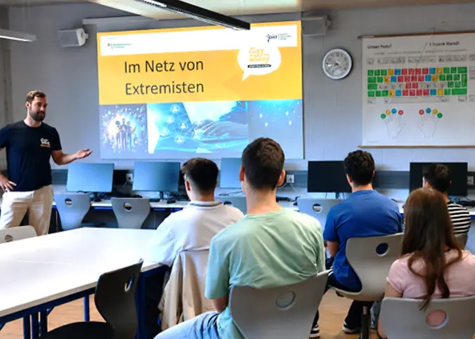 Ein Mann hält einen Vortrag dem 5 Schüler zuhören.