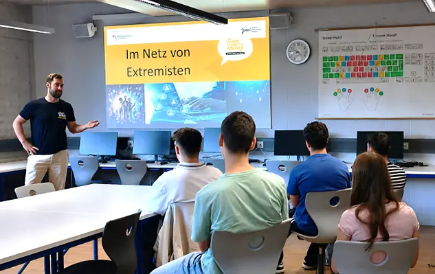 Ein Mann hält einen Vortrag dem 5 Schüler zuhören.