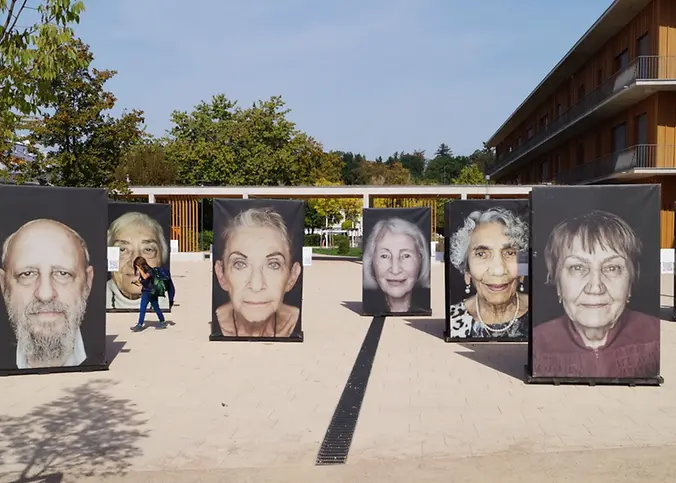 Sieben riesen große Porträts stehen auf einem Schulhof.