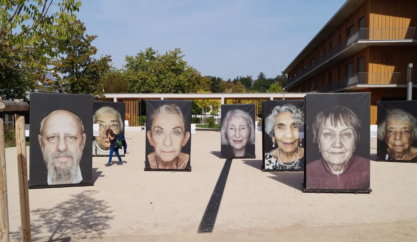 Sieben riesen große Porträts stehen auf einem Schulhof.